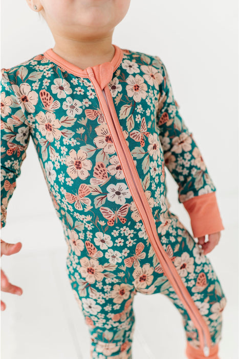 Baby wearing a floral and butterfly patterned onesie with a pink zipper on a white background
