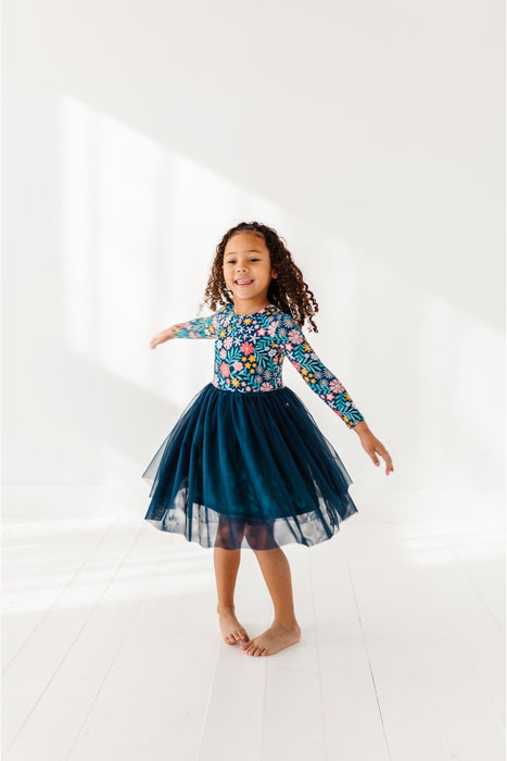 Young girl wearing a floral top and navy twirl tulle skirt on a white background