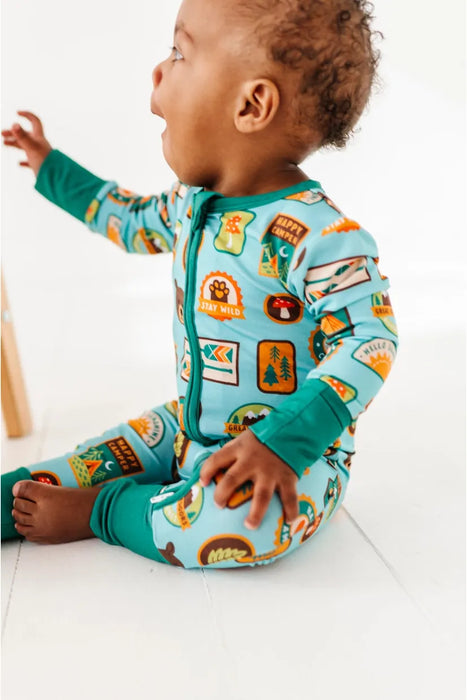 Baby model wearing bamboo zip up pajamas featuring bright, adorable illustrated adventure merit patches in Let's Explore print