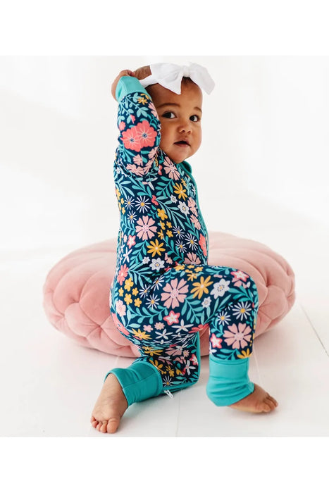 Side profile view of Smiling baby model in Maren Floral One Piece Zip Sleep Romper with pink flowers on navy background.