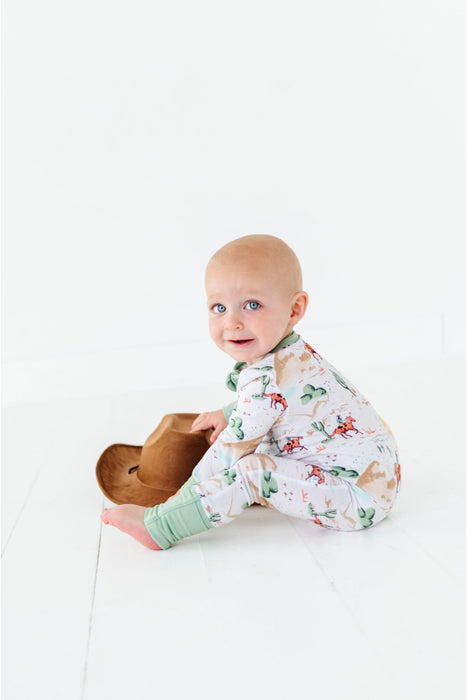 baby wearing billy western one piece zip sitting in studio with cowboy hat prop