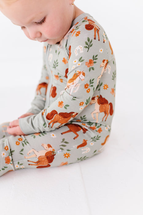 Baby wearing a long-sleeve zip PJ sleeper with horses pattern background  -Bird adn Bean Bamboo Baby Wear