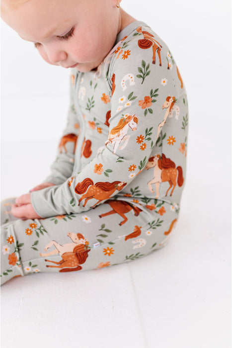 Baby wearing a long-sleeve zip PJ sleeper with horses pattern background  -Bird adn Bean Bamboo Baby Wear