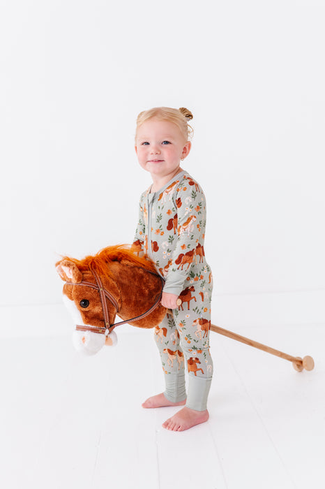 Child wearing a patterned horses print zip pajama  holding a plush toy horse on a white background  -Bird and Bean