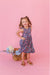 Young girl in a bamboo floral dress standing on a pink background with flowers in a basket | Bird and Bean Kids