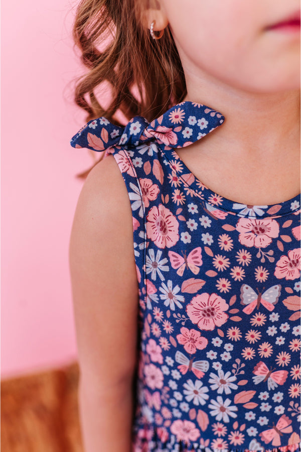 Child wearing a floral bamboo fabric dress  with bow tie shoulders with a pink background | Bird and Bean 