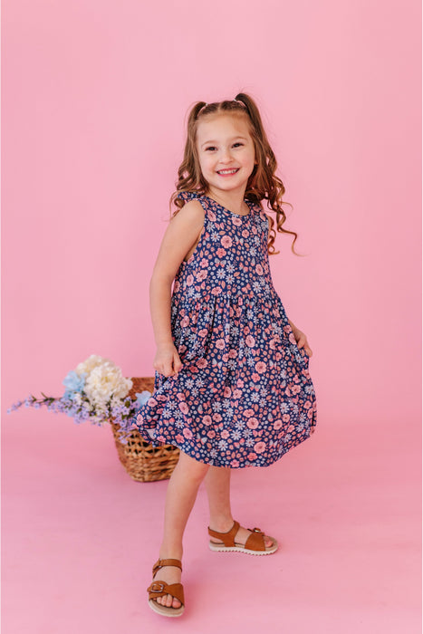 Young girl in a floral dress with twirly skirt standing against a pink background Bird and Bean Brand Dresses