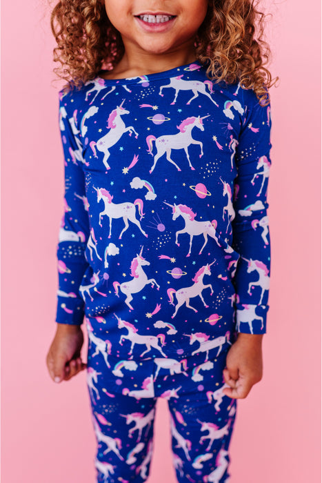 Child wearing a blue pajamas top and bottom with unicorn pattern on a pink background - Bird and Bean