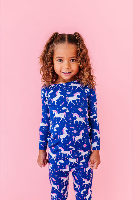 Child wearing a blue unicorn cosmic-patterned sleep pajamas set on a pink background  - Bird and Bean Kids Wear
