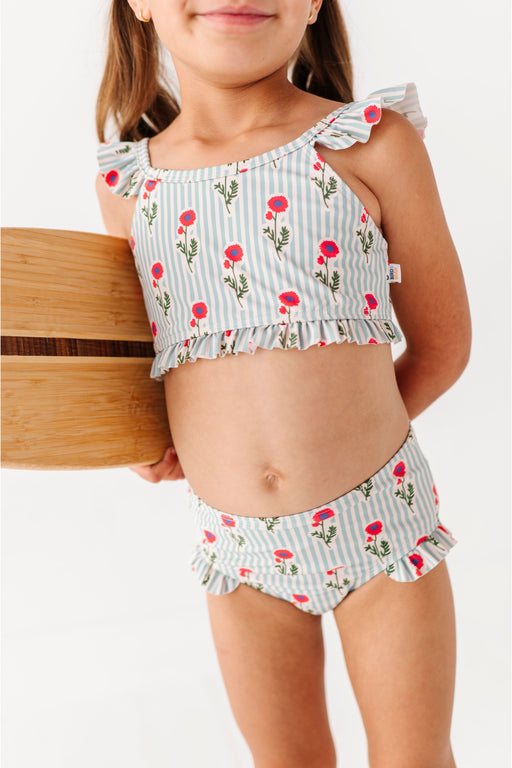 Child wearing a floral two-piece swimsuit holding a wooden basket on a white background Bird and Bean