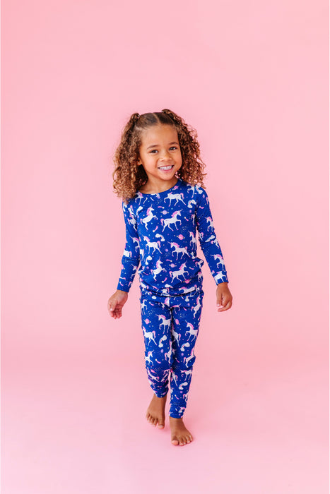 Child wearing a blue unicorn patterned outfit on a pink background - Bird and Bean PJs set 