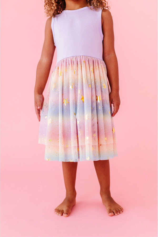 Child wearing a colorful rainbow tank tulle dress dress with lights on a pink background. Bird and Bean Kids 