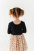 Child wearing a black top and beige skirt with black heart patterns on a white background | Bird and Bean Holiday Shop