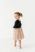 Young girl wearing a black top and beige polka dot skirt on a white background | Bird and Bean