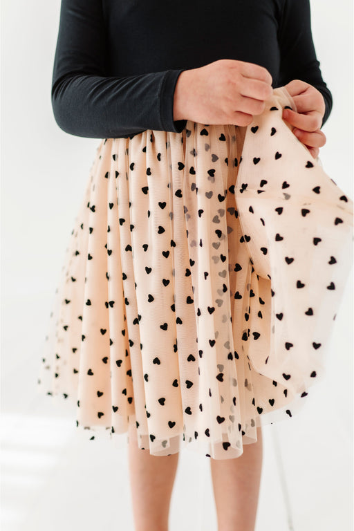 Girl wearing a beige tulle skirt with black heart patterns on a white background | Bird and Bean Holiday Shop