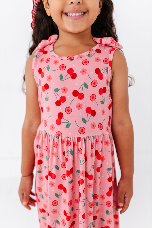 Young girl wearing a pink cherry print sundress, bamboo fabric on a white background | Bird and Bean Brand 