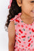 Child wearing a pink dress with bow shoulder tie with cherry pattern on a white background | Bird and Bean Kids