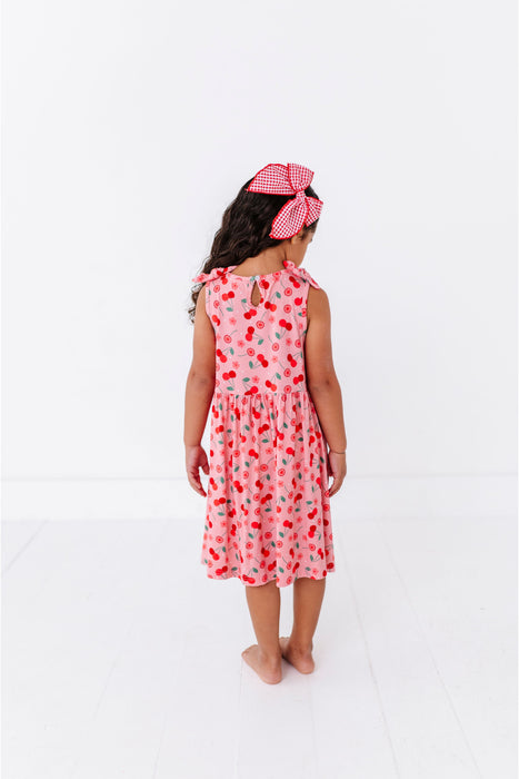 Young girl wearing a red cherry print midi length dress and headband on a white background - Bird and Bean