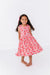 Young girl wearing a pink cherry print twirly bamboo fabric dress on a white background | Bird and Bean Dresses
