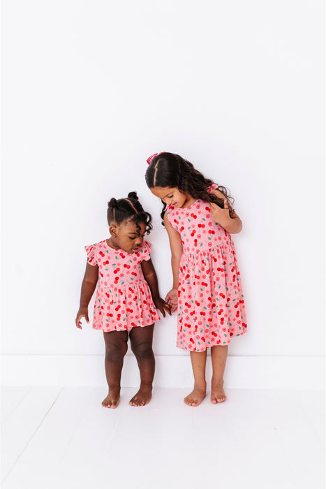 Two young girls wearing matching pink dresses with a cherry pattern bamboo fabric on a white background | BIrd and Bean Brand 