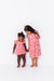 Two young girls wearing matching pink dresses with a cherry pattern bamboo fabric on a white background | BIrd and Bean Brand 