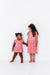 Two young girls wearing matching pink cherry print bamboo fabric dresses with a floral pattern on a white background - Bird and Bean Kids