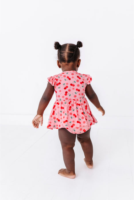 Baby girl wearing a pink cherry print dress, bamboo fabric on a white background | Bird and Bean Dresses