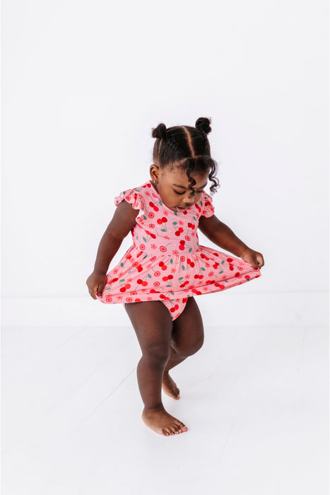 Young girl in a pink dress with red floral  and cherry pattern on a white background  Bird and Bean 