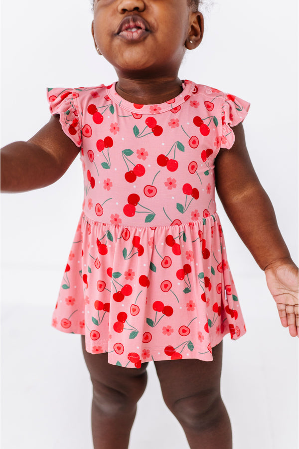 Child wearing a pink bamboo fabric dress with cherry pattern on a white background | Bird and Bean Kids 