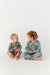 Two children in floral print matching PJs sitting on a white floor.