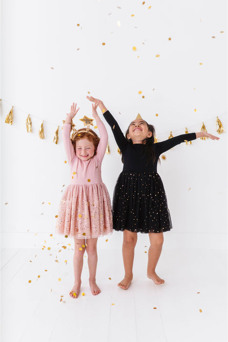 Two children in dresses standing with arms raised against a white background with gold confetti. | Bird and Bean Holiday Shop