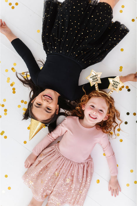 Two children lying on a white surface in B&B sparkly tulle dresses with gold confetti, wearing festive hats. | Bird and Bean Holiday Collection 