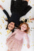 Two children lying on a white surface in B&B sparkly tulle dresses with gold confetti, wearing festive hats. | Bird and Bean Holiday Collection 