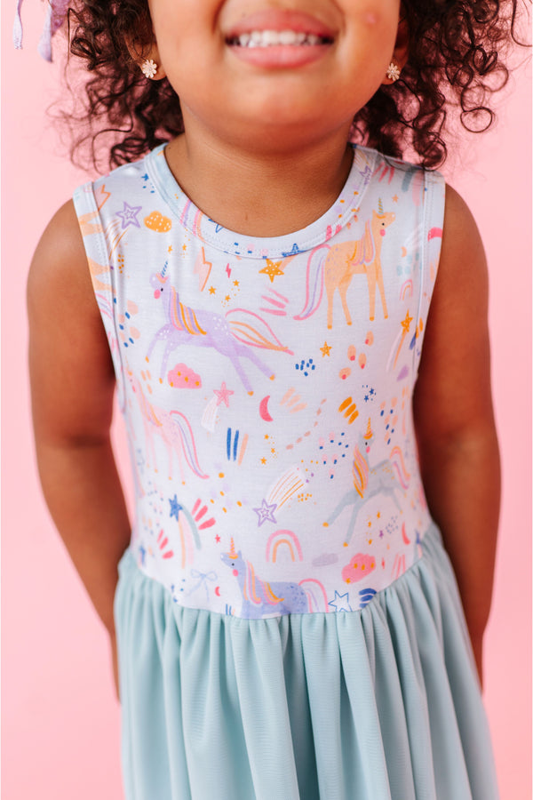Child wearing a colorful sleeveless unicorn  tulle dress  against a pink background Bird and Bean Kids