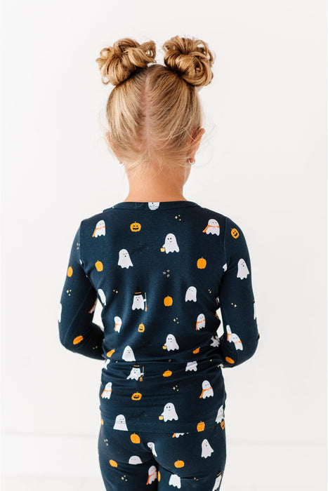 Child wearing a navy Halloween-themed outfit with ghosts, pumpkins, and ghosts on a white background