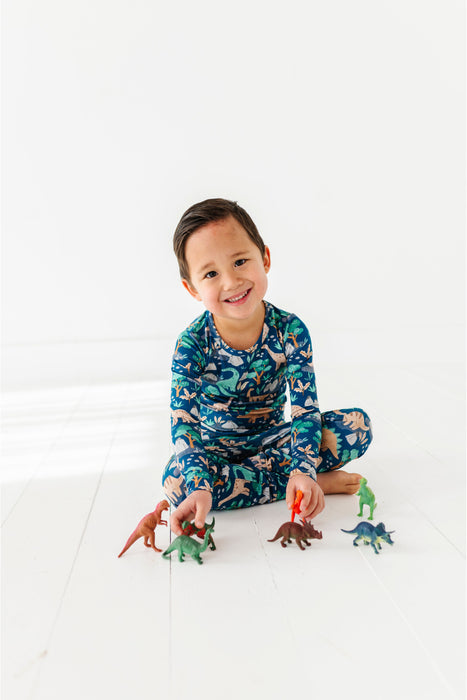 Child playing with toy dinosaurs wearing a dinosaur-themed bamboo pajamas set - Bird and Bean Kids Clothing