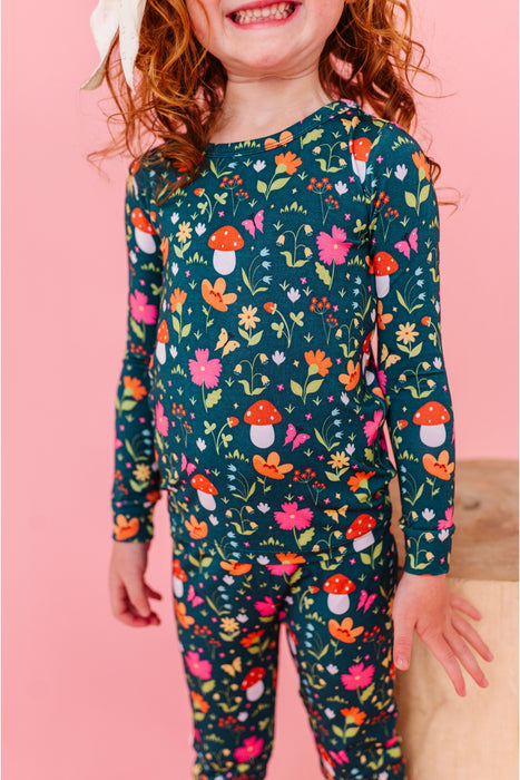 Child wearing a colorful floral and mushroom patterned outfit on a pink background | Bird and Bean