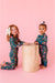 Two children in matching pajamas standing next to a wooden stool on a pink background | Bird and Bean