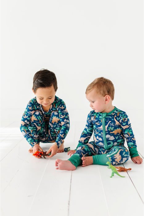 Two children in dinosaur-themed pajamas playing on a white floor. Bird and Bean Bamboo Kids Clothing Brand 