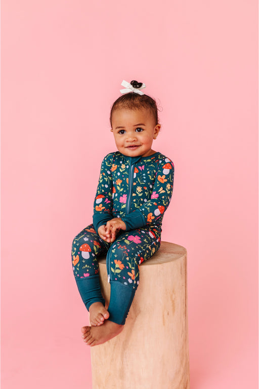 Baby sitting on a wooden block against a pink background wearing a floral zip pajamas | Bird and Bean 
