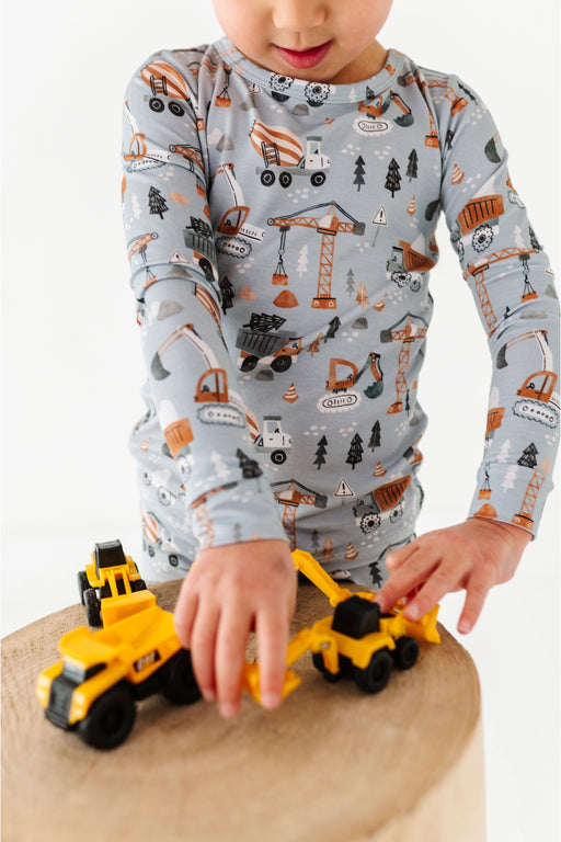 Child playing with toy construction vehicles wearing a long-sleeve shirt with a construction vehicle pattern. Bird and Bean PJs