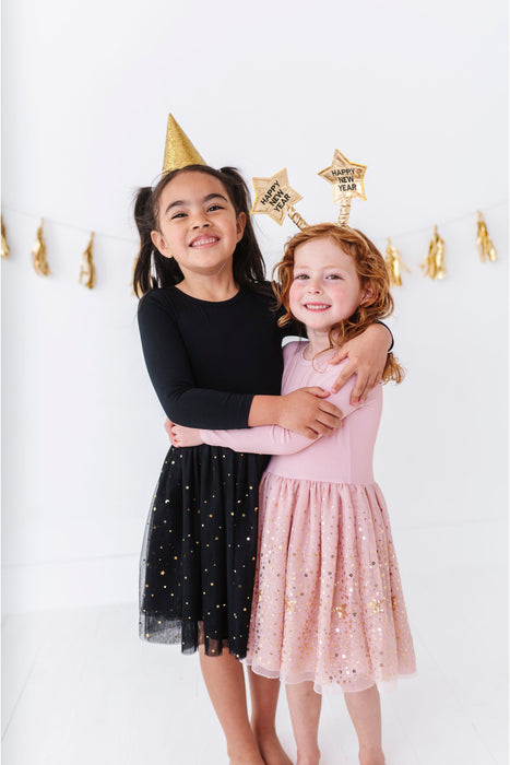 Two young girls wearing party dresses against a white background with gold decorations | Bird and Bean 