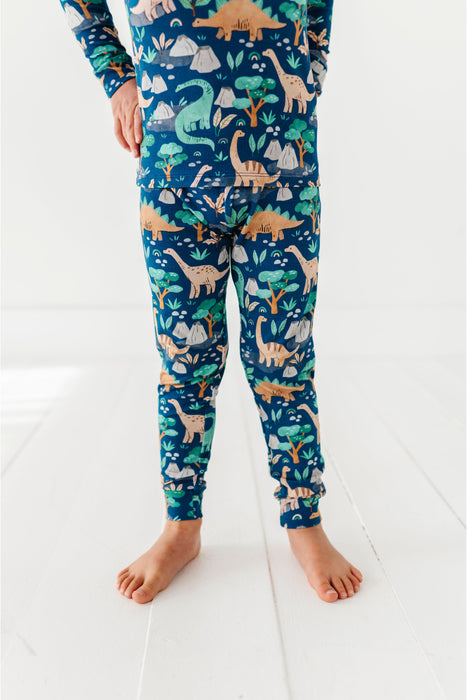 Child wearing dinosaur-themed pajama pants on a white floor. Bird and Bean PJ set. 