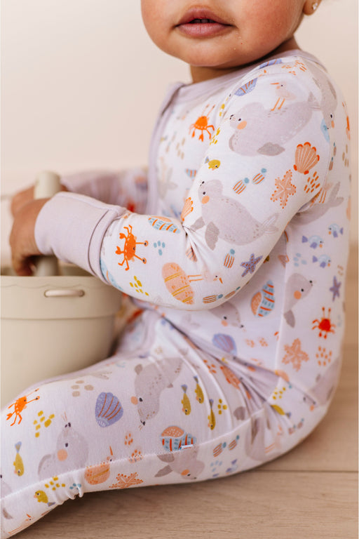 Child wearing a long-sleeve bamboo sleep zip romper with sea life animal prints sitting on a wooden floor. Bird and Bean Kids 