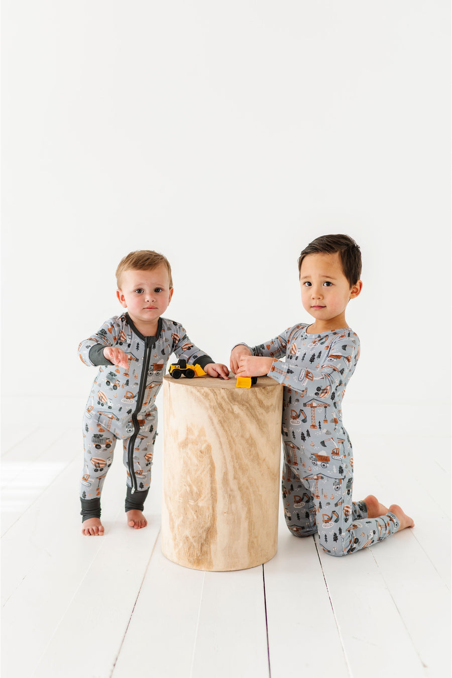 Two children in matching pajamas playing with a wooden block on a white floor. Bird and Bean 