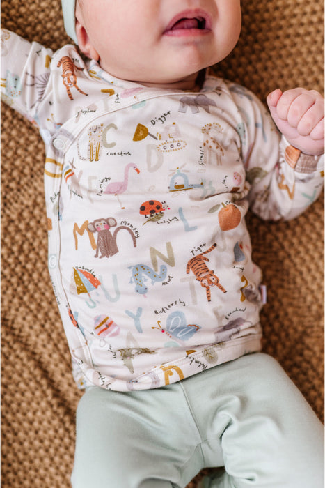 Baby wearing a long-sleeve shirt with animal and alphabet print on a textured surface. Bamboo Take Me Home Set – Animal ABC Bird and Bean Brand Original 