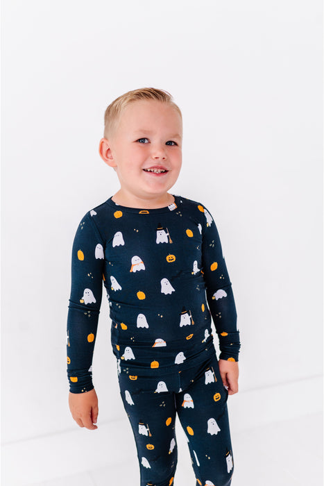 Child wearing a black long-sleeve Pajamas sleeve shirt and pants with ghost and pumpkin pattern on a white background. Bird and Bean