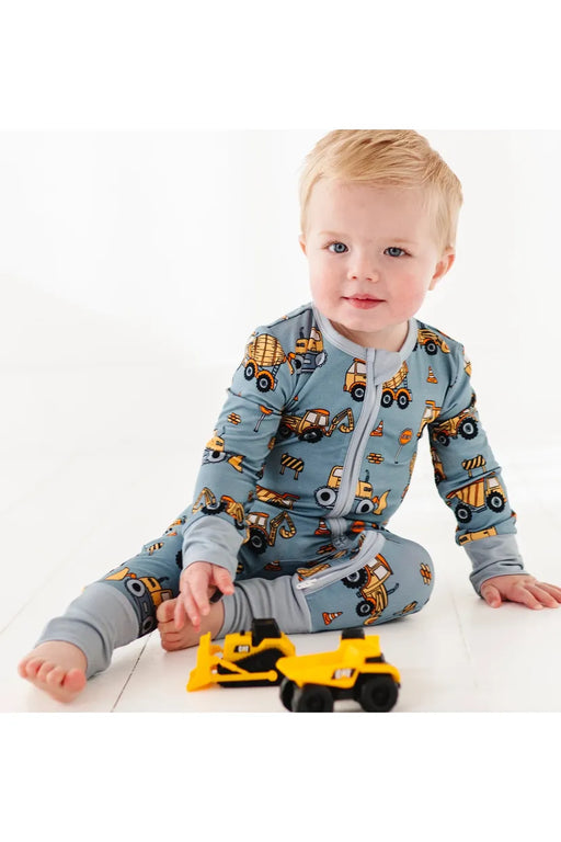 Baby model plays with toy trucks while wearing Construction Worksite Bamboo Zipper Pajamas with vehicles