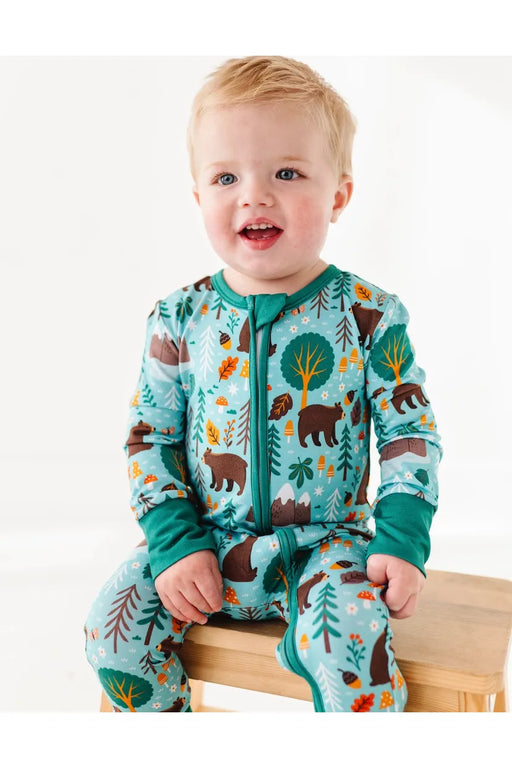 Baby model wears blue green bamboo pajama in Woody Woodland Bear print with mountains and mushrooms