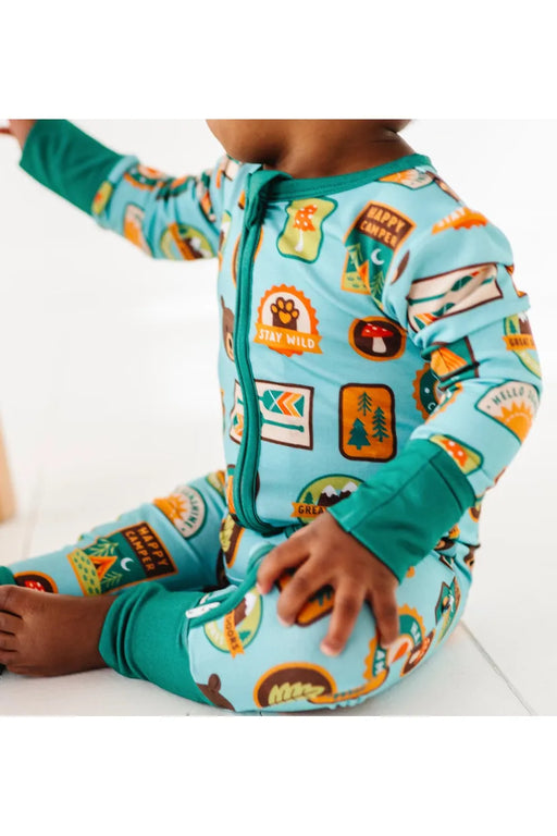 Close up of baby model wearing bamboo zip up pajamas featuring bright, adorable illustrated adventure merit patches in Let's Explore print